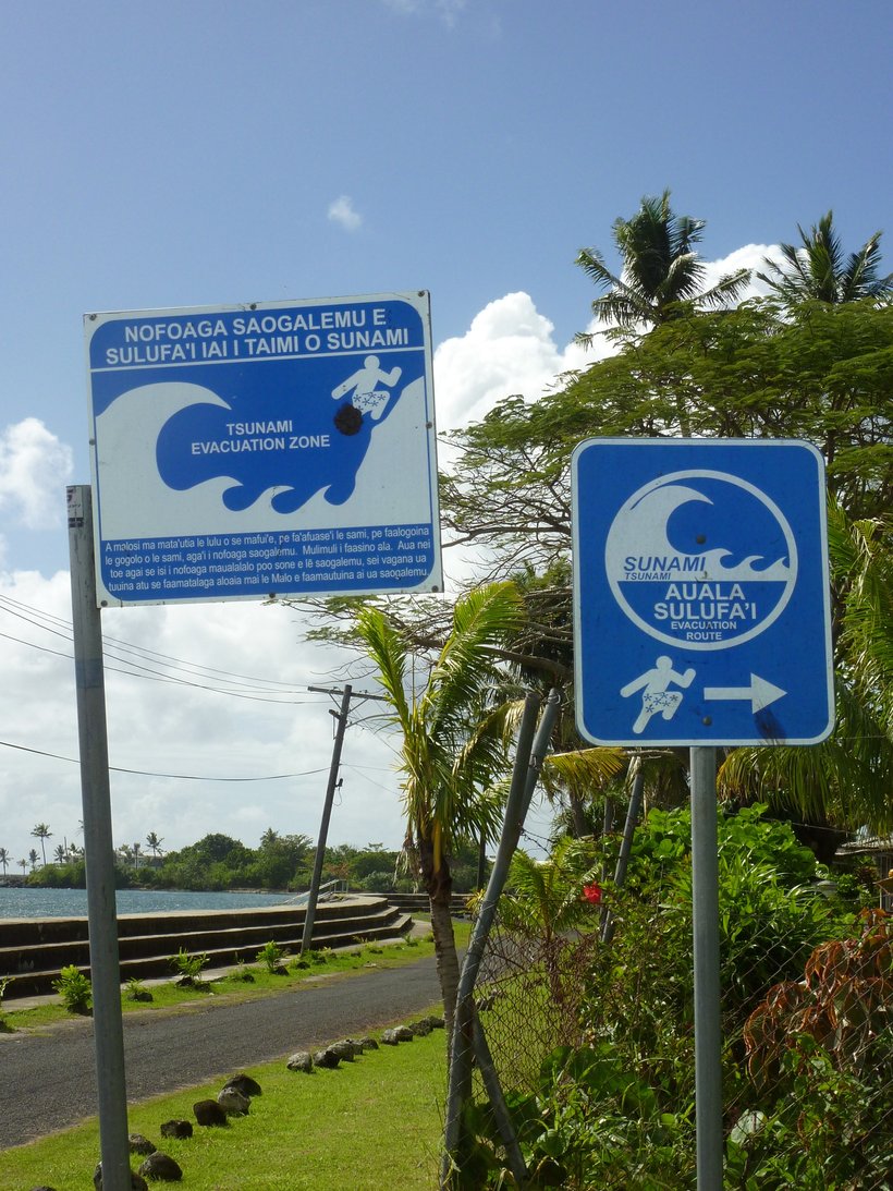 Tsunami warning signs by a beach in Samoa written in Samoan and English